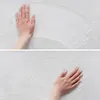 A person's hands are shown touching a white, textured surface, possibly demonstrating the softness or texture of a rug. Náhled obrázku produktu