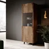 A modern wooden display cabinet with glass shelves is shown in a stylish living room setting, with a large window and a plant in the background. Náhled obrázku produktu