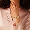 A woman wearing a pink satin shirt and a gold watch. Produktbild-Vorschau