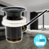 A black drain assembly with a lever, set against a blurred background of a modern bathroom. Produktbild-Vorschau