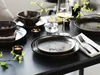 A table setting with plates, bowls, cutlery, a wine glass, and candles, decorated with greenery. Náhľad obrázku produktu