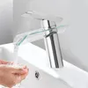 A modern chrome and glass waterfall faucet is shown in use, with water flowing into a person's hands in a sink. Podgląd zdjęcia produktu