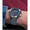 A close-up shot of a person wearing a silver Guess watch with a blue dial. Voir les images du produit