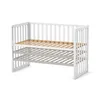 A white baby crib with a wooden slatted base, shown from a slightly elevated side angle against a white background. Anteprima dell’immagine prodotto