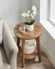 A round wooden side table with a white orchid in a pot and a glass of water on top, and a woven basket on the shelf below. Náhled obrázku produktu