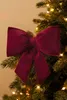 A close-up of a burgundy velvet bow on a Christmas tree with lights. Produktbild-Vorschau