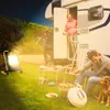 A man and a dog are relaxing by a camper van at night, with a bright LED work light illuminating the scene. Voir les images du produit