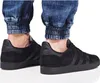 A close-up shot of a person's feet wearing black Adidas Gazelle sneakers and cuffed denim jeans. Voir les images du produit