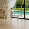 A transparent chair is placed next to a table set for a meal, with a swimming pool and greenery visible through a large window in the background. Produktbild-Vorschau
