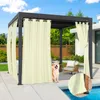 A dog sits near a pergola with beige curtains, next to a swimming pool.