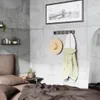 A bedroom scene with a coat rack holding a hat and jacket, a framed picture on the wall, and a bed in the foreground. Náhľad obrázku produktu