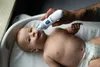 A person's tattooed arm is holding a white electric nasal aspirator to a baby's nose while the baby lies on its back in a white baby bath. Anteprima dell’immagine prodotto