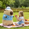 A young girl is having a picnic with a large capybara plush toy in a grassy park. Produktbild-Vorschau