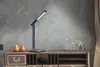 A modern desk lamp is displayed on a wooden desk with decorative items. Náhled obrázku produktu