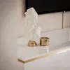 A white bust and a gold container sit on a white surface in front of a textured wall. Produktbild-Vorschau