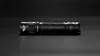 A black Nitecore MH12 Pro flashlight is shown on a black surface. Produktbild-Vorschau