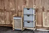 A bamboo laundry cart and a three-drawer storage unit are placed on a wooden floor in front of a rustic wooden door. Produktbild-Vorschau