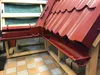 A close-up view of red metal roofing tiles and guttering components, displayed on a wooden frame. Produktbild-Vorschau