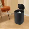 A black smart sensor trash can with its lid open, filled with crumpled paper, sits on a wooden floor next to an orange chair with a patterned pillow. Voir les images du produit