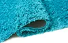 A close-up view of a rolled-up turquoise shaggy rug, showing the texture of the fibers and the underside of the rug. Produktbild-Vorschau