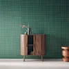 A wooden sideboard with sliding doors and a shelf, decorated with vases and a small stool, against a green grid-patterned wall. Produktbild-Vorschau
