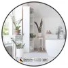 A round mirror with a black frame is shown in a bathroom setting, reflecting plants, shelves, and a bathtub. Produktbild-Vorschau
