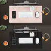 A split image showing two identical desk setups, one with a pink desk mat and one with a black desk mat, each featuring a monitor, keyboard, mouse, phone, headphones, and a cup of coffee. Produktbild-Vorschau