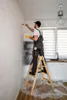 A man is painting a wall while standing on a ladder in a kitchen. Produktbild-Vorschau