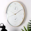 A wall clock with a white face, gold frame, and integrated thermometer and hygrometer, mounted on a white wall. Produktbild-Vorschau