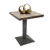 A square table with a wooden top and a dark metal base, decorated with three circular wooden planters containing small green plants.
