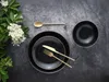 A table setting with black plates and gold cutlery, next to a sprig of white flowers. Náhľad obrázku produktu