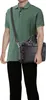 A person wearing a green polo shirt and black pants is holding a black briefcase. Produktbild-Vorschau
