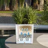 A white planter with a diagram showing its self-watering system is placed on a patio next to a swimming pool. Náhled obrázku produktu