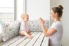 A mother and baby sitting on a wooden bench by a window, with decorative pillows. Produktbild-Vorschau