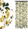 A close-up of a curtain fabric with a leaf pattern and a full curtain hanging.