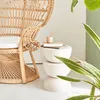 A rattan chair next to a stacked side table with books and a cup. Produktbild-Vorschau