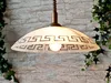 A pendant light fixture with a decorative pattern hangs against a brick wall background, with ivy vines on either side. Podgląd zdjęcia produktu
