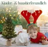 A young boy wearing reindeer antlers and a red sweater smiles while lying on the floor next to a small Christmas tree and a white dog. Anteprima dell’immagine prodotto