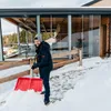 A man is shoveling snow in front of a modern house with large glass windows. Náhled obrázku produktu