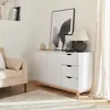 A white sideboard with wooden legs and accents, decorated with vases and framed pictures, is placed in a living room next to a beige armchair and a fluffy rug. Anteprima dell’immagine prodotto