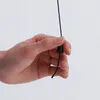 A hand is holding a black pull cord with a black conical knob on it. Produktbild-Vorschau