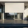 A beige vertical awning is extended over a modern patio with large glass doors and tiled flooring. Náhled obrázku produktu
