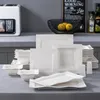 A collection of white porcelain dinnerware is displayed on a countertop, with kitchen appliances and decorative items in the background. Produktbild-Vorschau