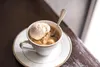 A cup of coffee with ice cream and a spoon on a saucer, placed on a wooden surface. Voir les images du produit