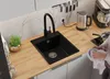 A person is drying a bowl next to a black kitchen sink and faucet on a wooden countertop. Produktbild-Vorschau