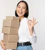 A woman is holding a stack of cardboard boxes and giving an okay sign. Náhľad obrázku produktu