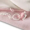 A close-up of a pink knitted blanket with a white plastic pacifier chain and a pink and white pacifier attached. Podgląd zdjęcia produktu