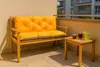 A wooden bench with an orange cushion and a small wooden table with drinks on a balcony. Produktbild-Vorschau