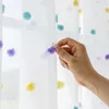 A hand is shown touching a pompom on a white curtain with colorful pompoms. Produktbild-Vorschau