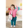 A baby girl is standing in a room, holding a stuffed animal. Podgląd zdjęcia produktu